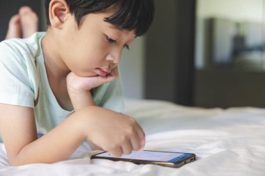 Siyah kâküllü Asyalı çocuğun yakın portresi, gülümseyen yüzlü, açık yeşil tişörtlü, akıllı telefonuyla oynayan Asyalı çocuk. Eğitim kavramı.