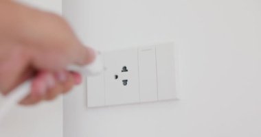 Adamın eli fişe takılı ve ofisteki bir elektrik cihazının fişini çekiyor. Beyaz bir elektrik prizi ve bir ışık düğmesi. Çözüm videosu 4K. Teknoloji kavramı, bağlantı, güç tasarrufu, enerji tasarrufu