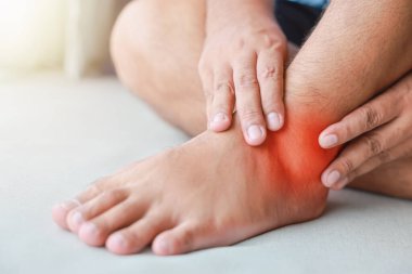 Bir adam ayak bileğini incitti ve o şişmiş ve kırmızıydı. Ağrı nedenleri arasında ayak bileği burkulması, gut, romatizma, ofis sendromu, uyuşukluk ve kramp belirtileri var. Sağlık hizmetleri tıbbi konsepti.