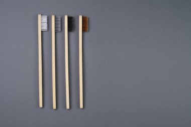 Three eco-friendly bamboo toothbrushes are arranged neatly on a solid gray background. The toothbrushes are unmarked and show the natural grain of the bamboo material. clipart