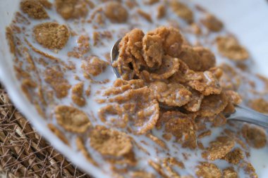 Tahta bir masada duran gümüş kaşıkla mısır gevreği ve sütle dolu bir kase..