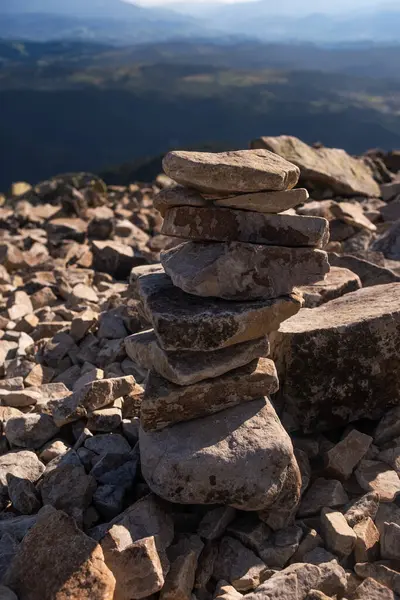 stock image A stack of rocks is positioned on a rocky mountain surface, surrounded by distant hills and clear skies in the background.