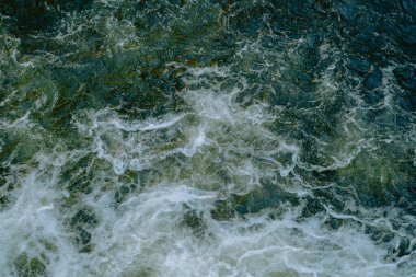 Çalkantılı okyanus dalgaları, karanlık bir gökyüzünün altında kayalık kıyılara çarpan beyaz köpük oluşturur..