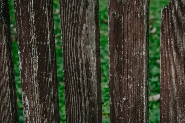 stock image A rustic, weathered wooden fence with varying textures, separated by gaps, stands against vibrant green grass.