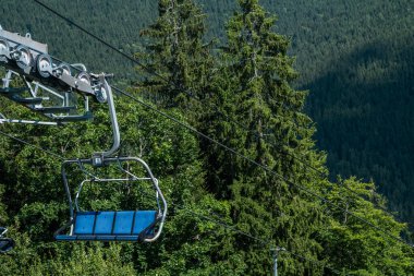 The chairlift climbs steadily, offering views of dense foliage and distant peaks under a clear sky. clipart