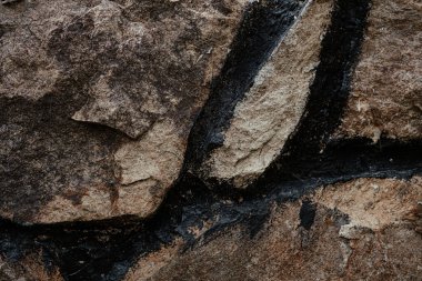 Yakından bakıldığında, doğal dokular arasında belirgin koyu mineral çizgileri olan kayalık bir yüzey, engebeli bir açık hava ortamında jeolojik oluşumları vurguluyor..