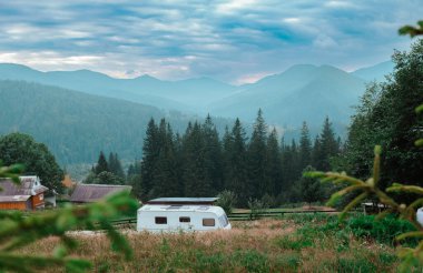 Beyaz bir kervan, yemyeşil bir vadide huzur içinde oturur. Yükselen ağaçlar ve sabah sisi ile örtülü uzak dağlarla. Huzurlu bir atmosfer yaratır..