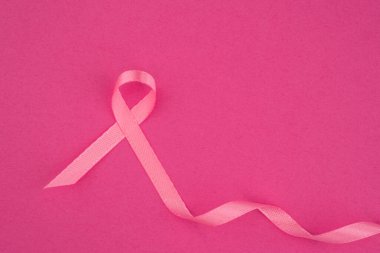 Pembe bir kurdele, göğüs kanseri farkındalığını temsil eden açık pembe bir arka planda sergileniyor..