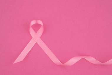 Göğüs kanseri farkındalığını temsil eden pembe bir kurdele yumuşak pembe bir arka planda zarifçe yatıyor..
