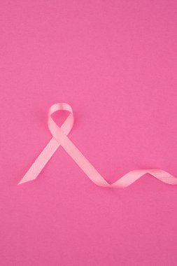 Pembe bir kurdele canlı pembe bir arkaplanda duruyor, bu da meme kanseri farkındalığını temsil ediyor..