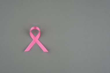 Pembe bir kurdele, göğüs kanseri farkındalığını ve destek çabalarını temsil eden gri bir arkaplanda oturur..