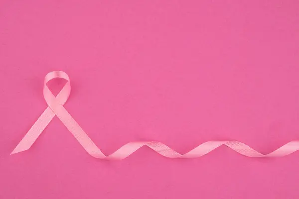 stock image A pink ribbon on a soft pink backdrop highlights breast cancer awareness.