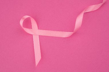 Pembe bir kurdele canlı pembe bir arka planda zarifçe sergilenir, farkındalığı temsil eder..