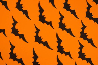 Colorful bats spread across an orange background, creating a festive Halloween atmosphere. clipart