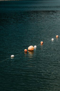 Various colorful buoys are floating on the tranquil surface of the lake as the sun sets in the background, creating a peaceful atmosphere. clipart