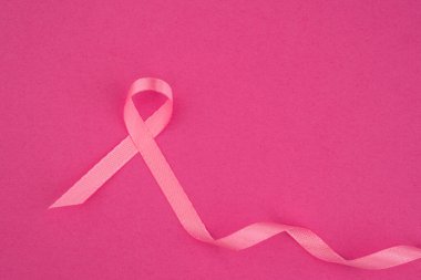 Pembe bir kurdele, göğüs kanseri farkındalığını temsil eden açık pembe bir arka planda sergileniyor..