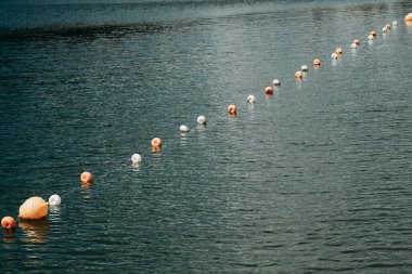 Şamandıralar gölün sakin yüzeyinde, şafağın yumuşak renklerini yansıtan ve çevrenin doğal güzelliğini artıran düzgün bir çizgide yüzerler..