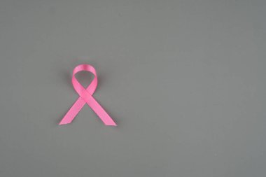 Pembe bir kurdele, göğüs kanseri farkındalığını ve destek çabalarını temsil eden gri bir arkaplanda oturur..