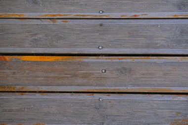 Yüzeyde, aşınma ve kullanım belirtileri gösteren oyuklar ve çizikler olan eski tahta güverte tahtaları yer alıyor. Çeşitli tonlar kahverengi ve gri kırsal bir görünüm yaratır, bu da uzun süre açık havada kalmalarını sağlar..