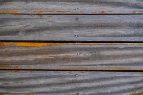 Yüzeyde, aşınma ve kullanım belirtileri gösteren oyuklar ve çizikler olan eski tahta güverte tahtaları yer alıyor. Çeşitli tonlar kahverengi ve gri kırsal bir görünüm yaratır, bu da uzun süre açık havada kalmalarını sağlar..