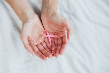 Eller, meme kanseri farkındalığı ve destek çabaları için kullanılan pembe kurdeleyi nazikçe tutuyor..