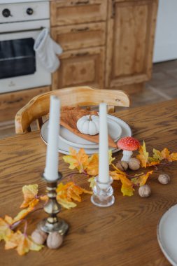 Mumlar, balkabakları ve ahşap bir masanın üzerindeki renkli yapraklarla sıcak bir sonbahar yemeği düzenlemesi..