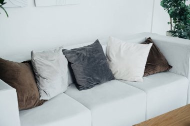 Parlak bir odada çeşitli renklerde dekoratif yastıklarla süslenmiş modern beyaz bir kanepe bulunur..