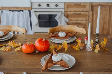 A beautifully set dining table showcases small pumpkins and vibrant autumn leaves. clipart