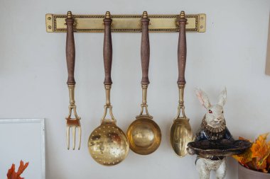 Antique kitchen utensils hang on a wall, complemented by a whimsical rabbit figurine nearby. clipart