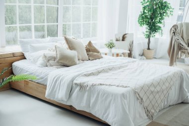 Geniş bir yatak odasında yumuşak çarşafları, yastıkları ve güneş ışığıyla yıkanmış bitkileri olan büyük bir yatak odası vardır..