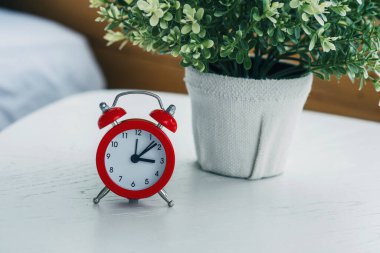 Kırmızı alarm saati, beyaz bir masada, yeşil bir saksı bitkisinin yanına yerleştirilmiş..