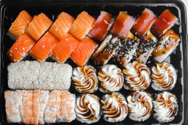 Suşi ruloları ve kremalı tatlılar güzel bir şekilde siyah tepside dizilmiş, çeşitliliklerini sergiliyorlar..