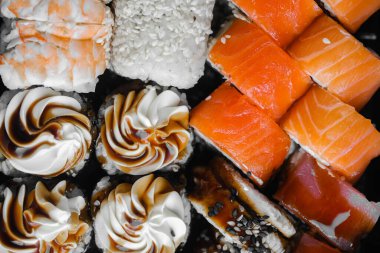 Cazip bir suşi çeşitliliği ve tatlı ruloları koyu bir tabakta sergileniyor, canlı renkler sergileniyor..