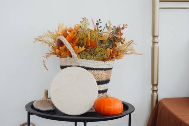 Sonbahar yaprakları ve çiçeklerle dolu dekoratif bir sepet masada bir balkabağının yanında oturur..