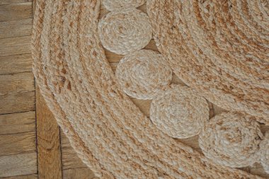 Dairesel desenli dokulu bir halı, yumuşak bir şekilde aydınlatılmış, sıcak ahşap bir zeminde yatıyor..