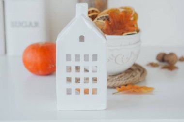 Ev şeklinde beyaz bir seramik fener sonbahar dekoru olan bir masada oturur..