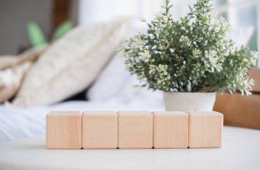 A series of four wooden cubes lined up on a table accompanied by a small potted plant. The background features a light and airy living room with soft furnishings. clipart