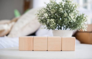 Dört ahşap bloktan oluşan bir set, arka planda küçük bir saksı bitkisi ile tamamlanmış bir sehpanın üzerinde düzgün bir şekilde düzenlenir ve kapalı bir yerde rahat bir atmosfer yaratır..