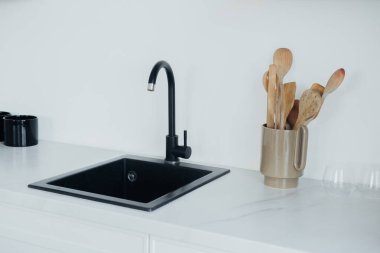 Parlak siyah bir lavabo, içinde ahşap kaplar bulunan seramik bir kapla tamamlanır. Tezgah, çağdaş mutfaklar için mükemmel minimalist bir tasarım sergiliyor..