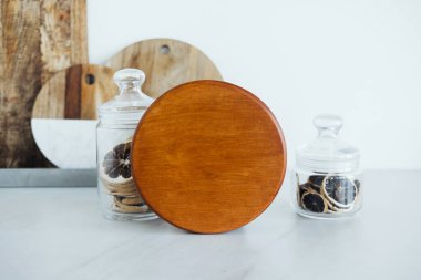 Kurumuş narenciye dilimlerinin bulunduğu iki cam kavanozun önüne bir tahta kesme tahtası konur. Doğal elementlerle dolu temiz ve modern bir mutfak düzeneği sergilenir..