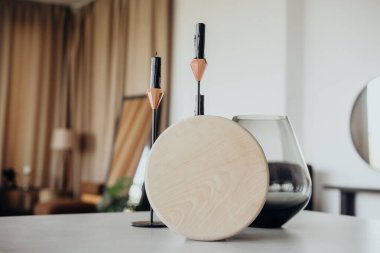 Yuvarlak bir ahşap süs ve parlak mum tutacakları, parlak ve havadar bir oturma odasında, koyu cam bir vazoyla tamamlanmış minimalist bir masanın üzerinde zarif bir şekilde otururlar..