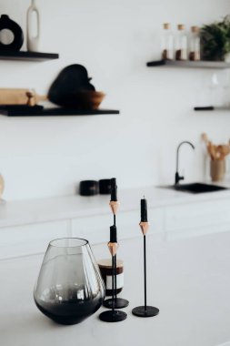 Modern bir mutfakta kendine özgü cam bir vazoyla tamamlanmış siyah mumları olan zarif mum tutucuları bulunur. Minimalist tasarım elementleri uzayın genel estetiğini geliştirir.