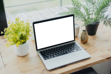 Modern bir çalışma alanı, canlı yeşil bitkiler ve yumuşak doğal ışıkla aydınlatılmış dekoratif bir vazoyla çevrili ahşap bir masanın üzerinde parlak bir dizüstü bilgisayar içerir..