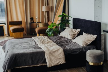 Şık bir yatak odası yumuşak çarşaflı büyük bir yatak odası, kapalı bir bitki ve sıcak bir ışık barındırır. Doğal ışık perdelerin arasından boşluğu doldurur ve karşılayıcı bir atmosfer yaratır..