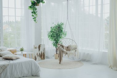 Konforlu yaşam alanında yeşil alanlarla çevrili, geniş pencereli, doğal ışık alan sallanan bir sandalye yer alıyor. Yumuşak tekstil sıcak bir dokunuş ekler, dingin bir atmosfer yaratır..