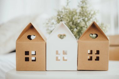 Üç dekoratif kutu ev şeklinde, bronz ve beyaz, bir ışık masasına yerleştiriliyor. Yumuşak doğal ışık odayı dolduruyor, taze, minimalist dekoru arttırıyor..