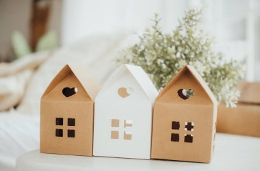 Kartondan yapılmış üç küçük dekoratif ev parlak bir masanın üzerinde sergileniyor, yanında zarif bir buket, rahat bir ortamda büyüleyici bir atmosfer yaratıyor..