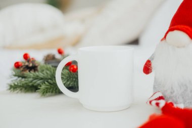 Neşeli bir Noel Baba figürü boş bir fincanın yanında oturur. Çam ve böğürtlenlerle süslenmiş bir masada. Sıcak, davetkar bir ortamda sıcak bir tatil sabahının özünü yakalar..