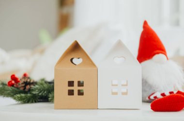 Kahverengi ve beyaz renkli iki büyüleyici kağıt ev tuhaf bir cücenin yanında oturuyor. Şenlikli yeşilliklerle düzenlenmişler. Tatil için mükemmel bir kış atmosferi yaratıyorlar..