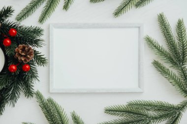 Boş beyaz bir çerçeve sonsuz yeşil dallar, çam kozalakları ve kırmızı süsler arasına yerleştirilir ve tatil gösterileri veya davetiyeler için mükemmel konforlu ve şenlikli bir atmosfer yaratır..